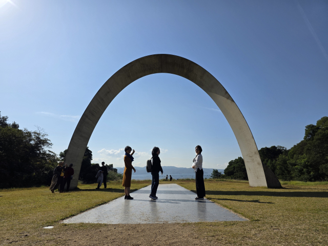 일본 나오시마 세토내해 언덕과 바다 사이에 설치돼 있는 이우환 작가의 ‘무한문’ 아래에서 기념사진을 찍는 방문객 모습. 이우환 미술관 야외 설치 작품 중 하나이다. 고재희 제공
