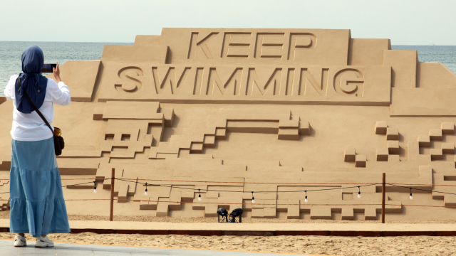 9일 부산 해운대해수욕장을 찾은 관광객이 방탄소년단(BTS) 신곡 'KEEP SWIMMING'이 적힌 대형 모래 작품을 사진 촬영하고 있다. 연합뉴스