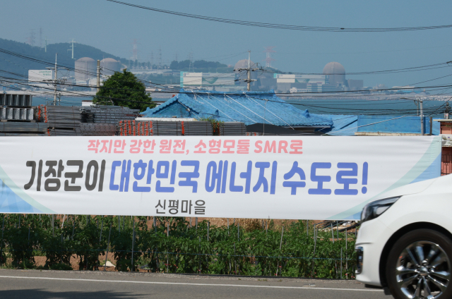 한국수력원자력이 신규 원전 건설을 위한 후보 부지로 대형원전 2기는 경북 영덕군, SMR 1기는 기장군을 확정했다고 밝힌 가운데 18일 부산 기장군 신평마을회관 인근 도로변에 내걸린 SMR 기장군 유치를 희망하는 내용의 현수막 뒤로 고리 1, 2, 3, 4호기가 보인다. 연합뉴스